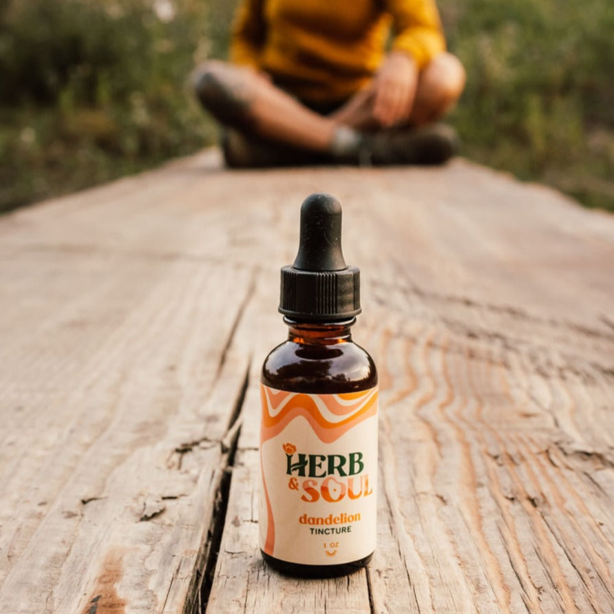 Herb & Soul Dandelion tincture on wooden plank with a woman seating in the background